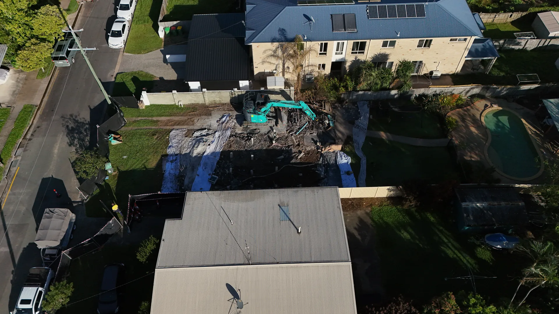 Aerial view of house demolition site with excavator.